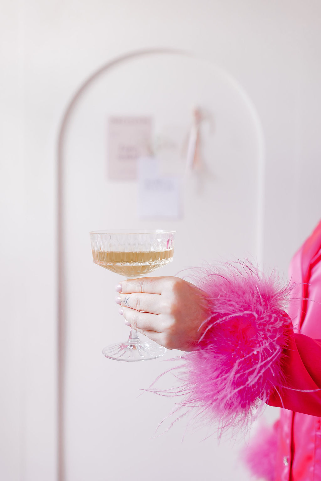 Champagnerschale in der Hand mit pinken Federärmeln